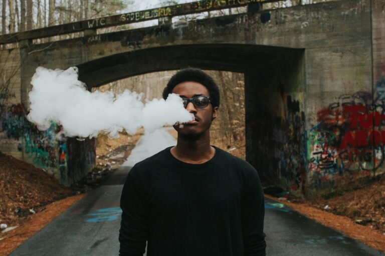 Portrait of a stylish young man smoking under a graffiti-covered bridge, adding urban flair.